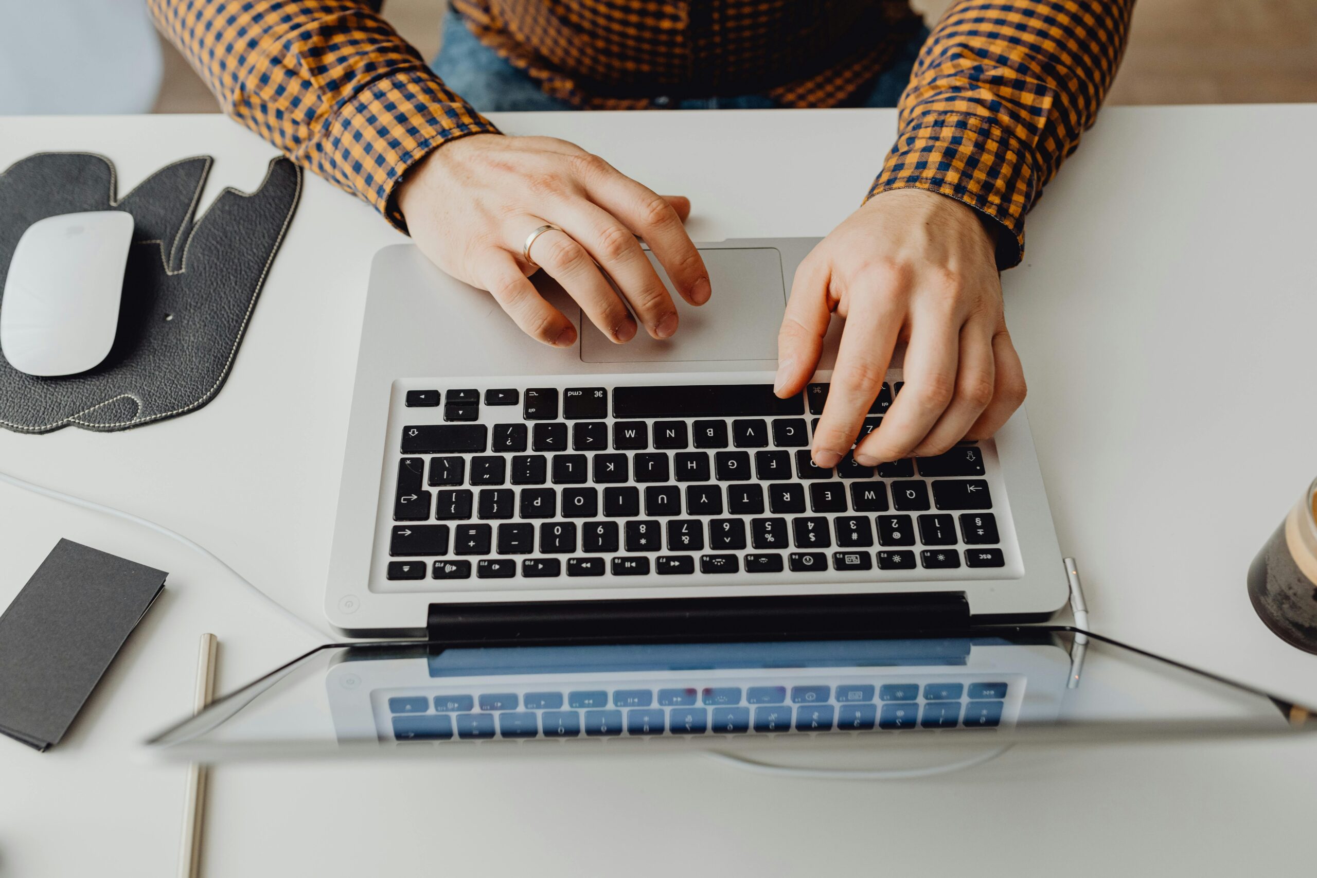 view of hands typing on a silver laptop keyboard on a white desk